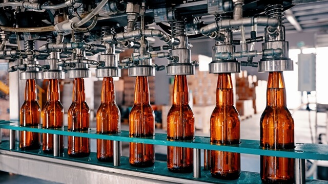Row of amber glass beer bottles being filled on an automated production line in a brewery.