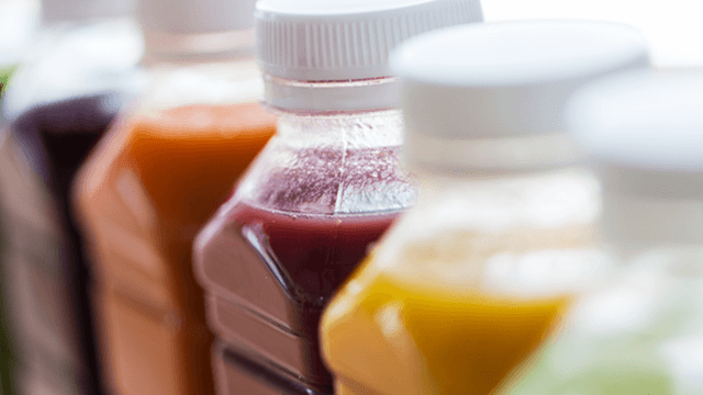 Close up of assorted colorful juice bottles with white caps, arranged in a row
